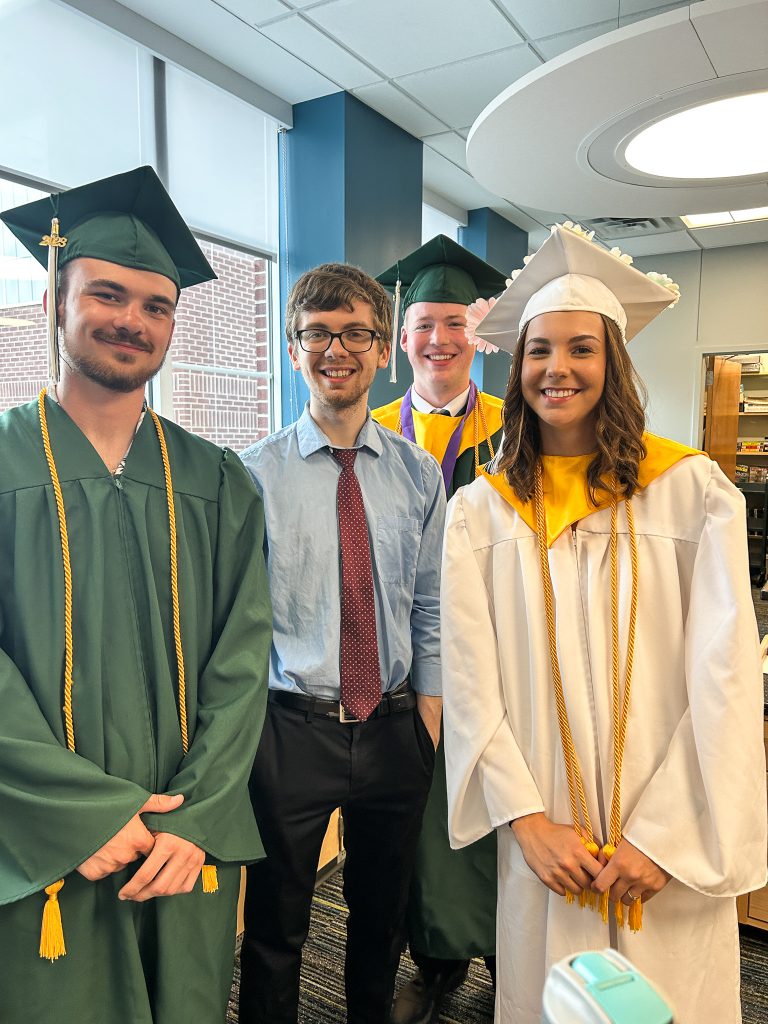 Students in cap and gown stand with teacher