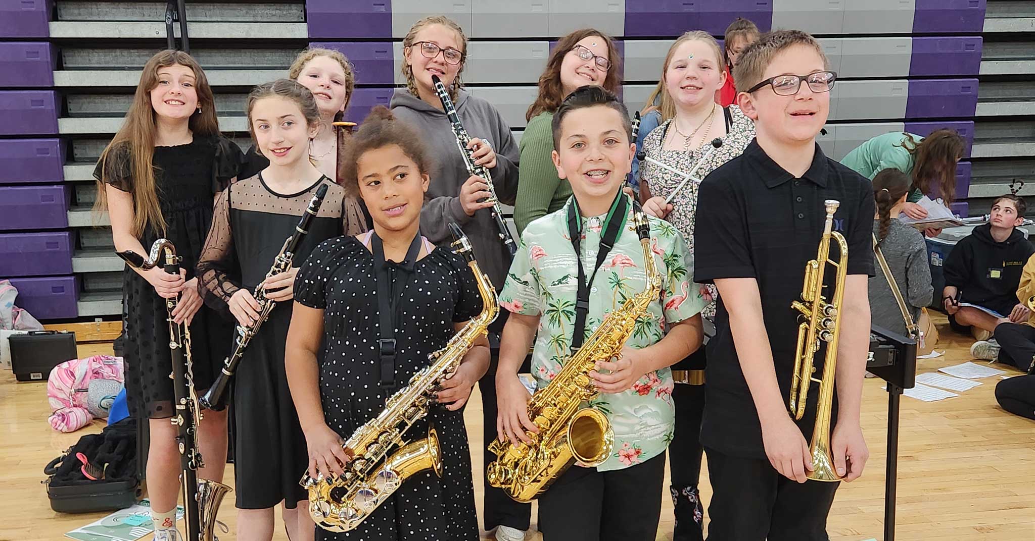 Members of the elementary band, wearing concert attire stand together. Many are holding their instruments.
