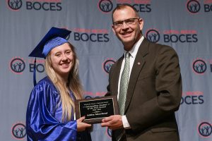 Student in cap and gown accepts award from man.