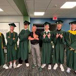 Students in cap and gowns. Coach is at the center.