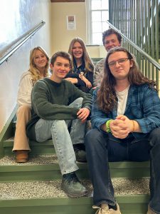 Five students sit on school stairs.