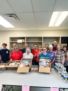 Volunteers stand behind boxes and cans of food.