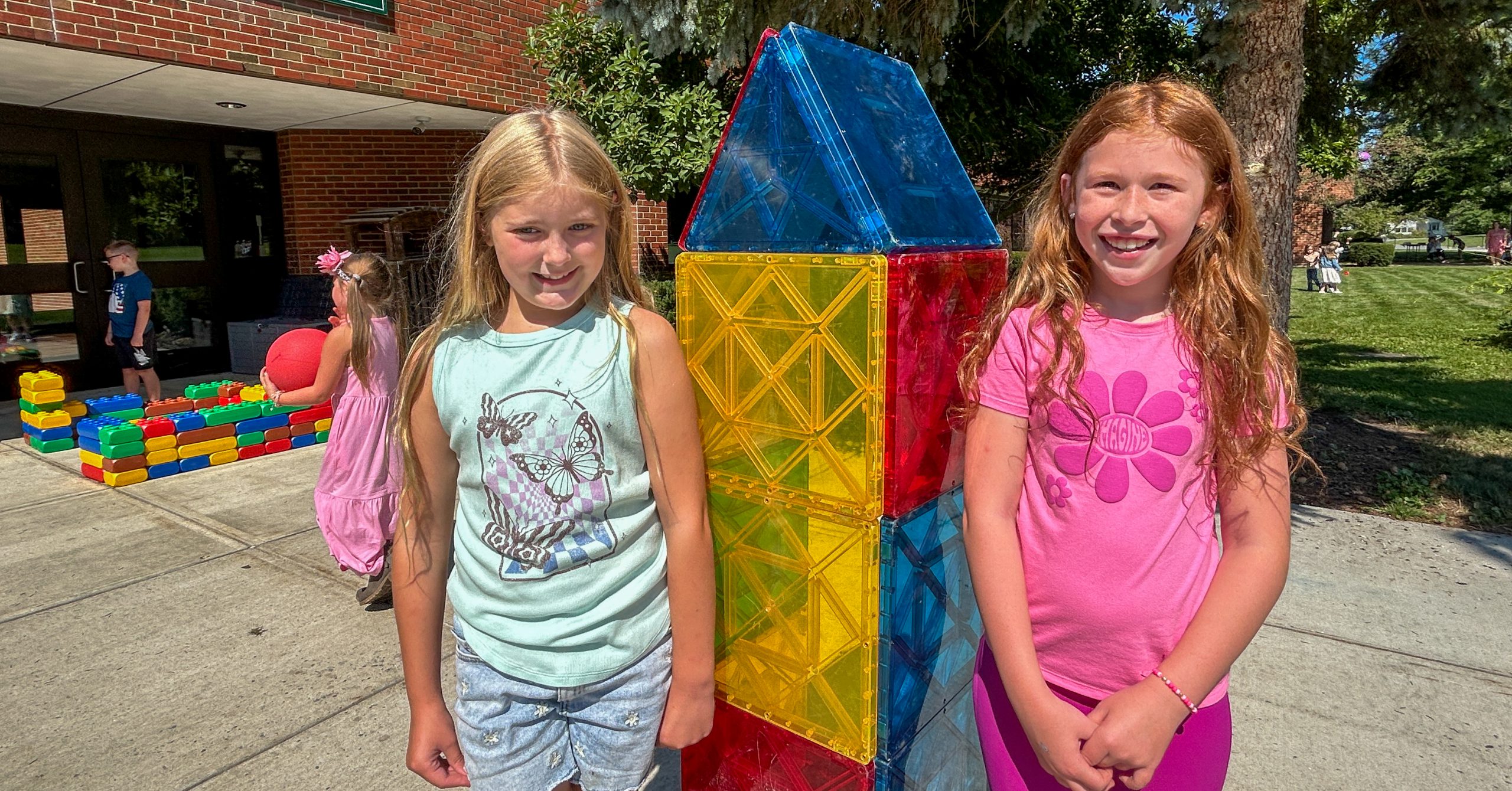 Two girls stand next to building structure outside of elementary building.