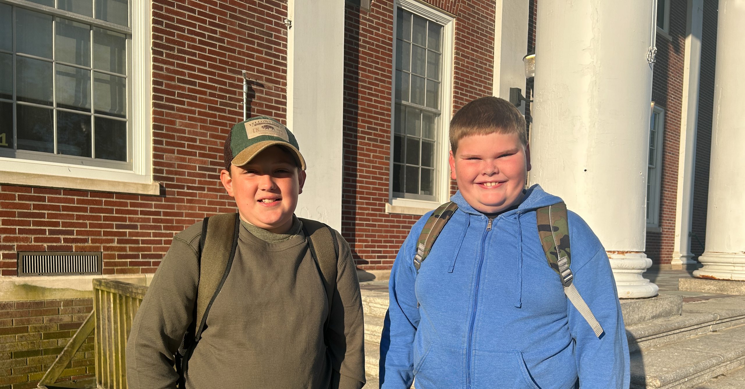 Two junior high students stand in front of school.