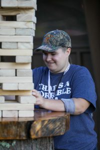 Teen wearing a camo hat and a t-shirt manipulates large, stacked, wooden blocks.