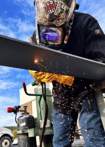 Student, wearing a helmet, welds a piece of metal.