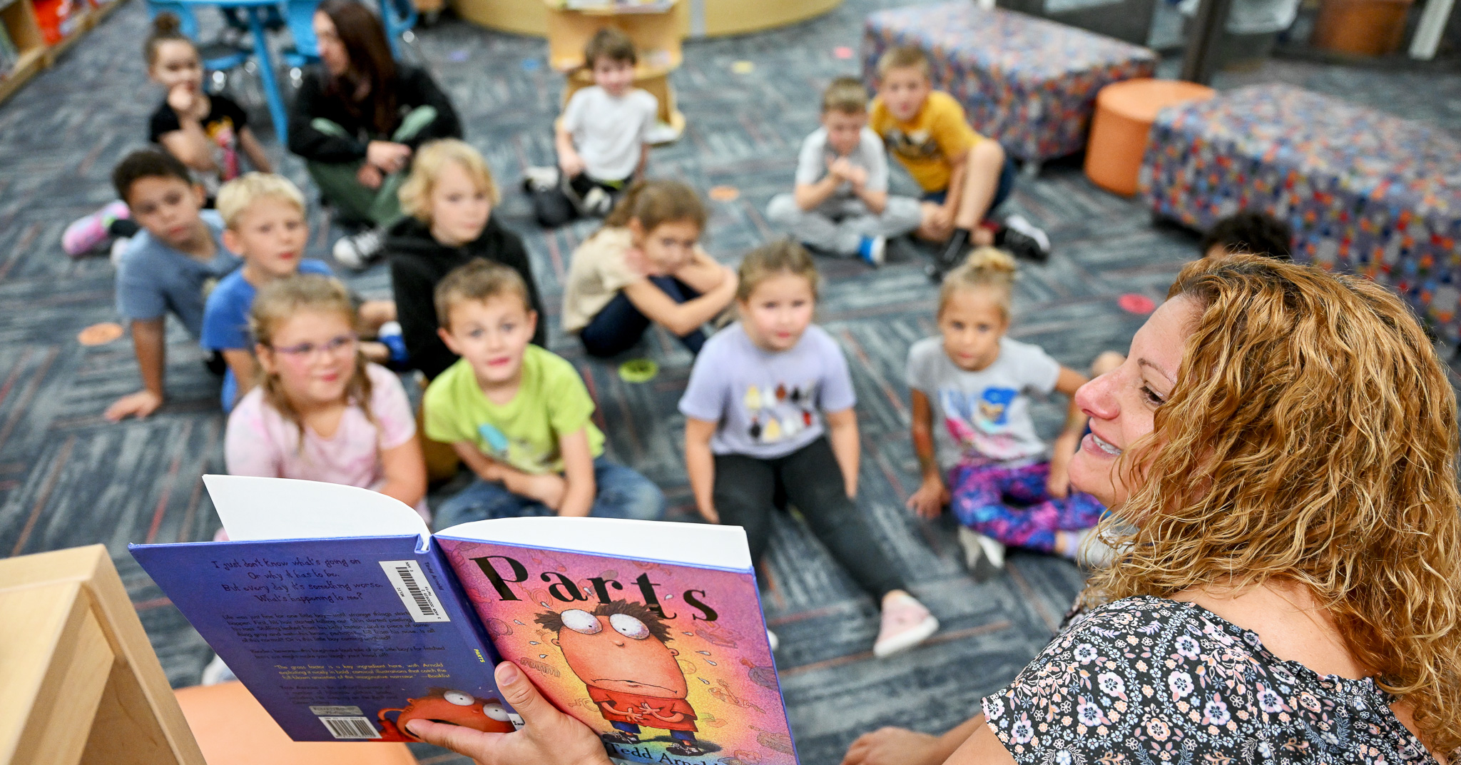 Librarian reads a book called Parts to students who are sitting on a rug.