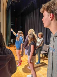 Six students acting on stage. One is pointing up.