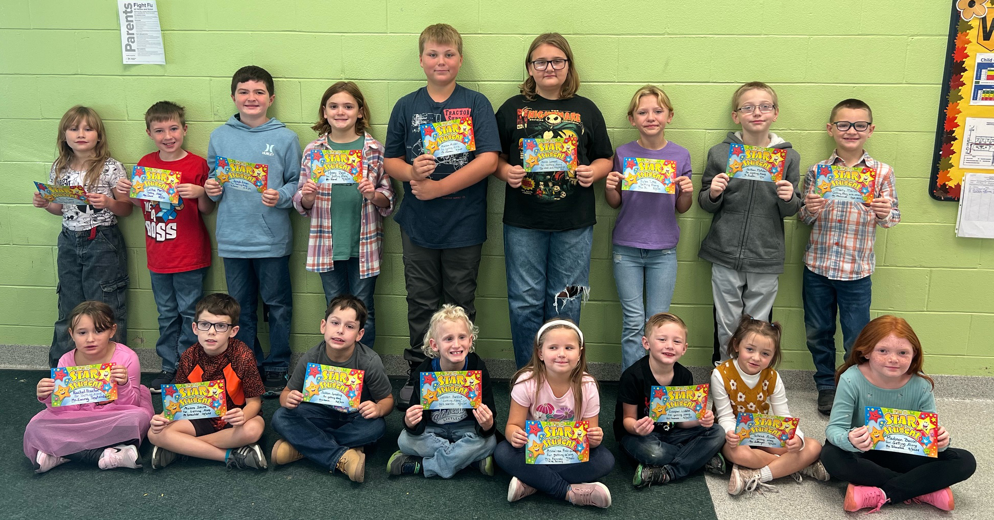 Group of elementary students, some sitting and some standing. Each is holding an achievement certificate.