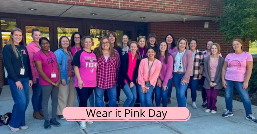 Twenty women, each wearing pink, stand in front of entrance to school.