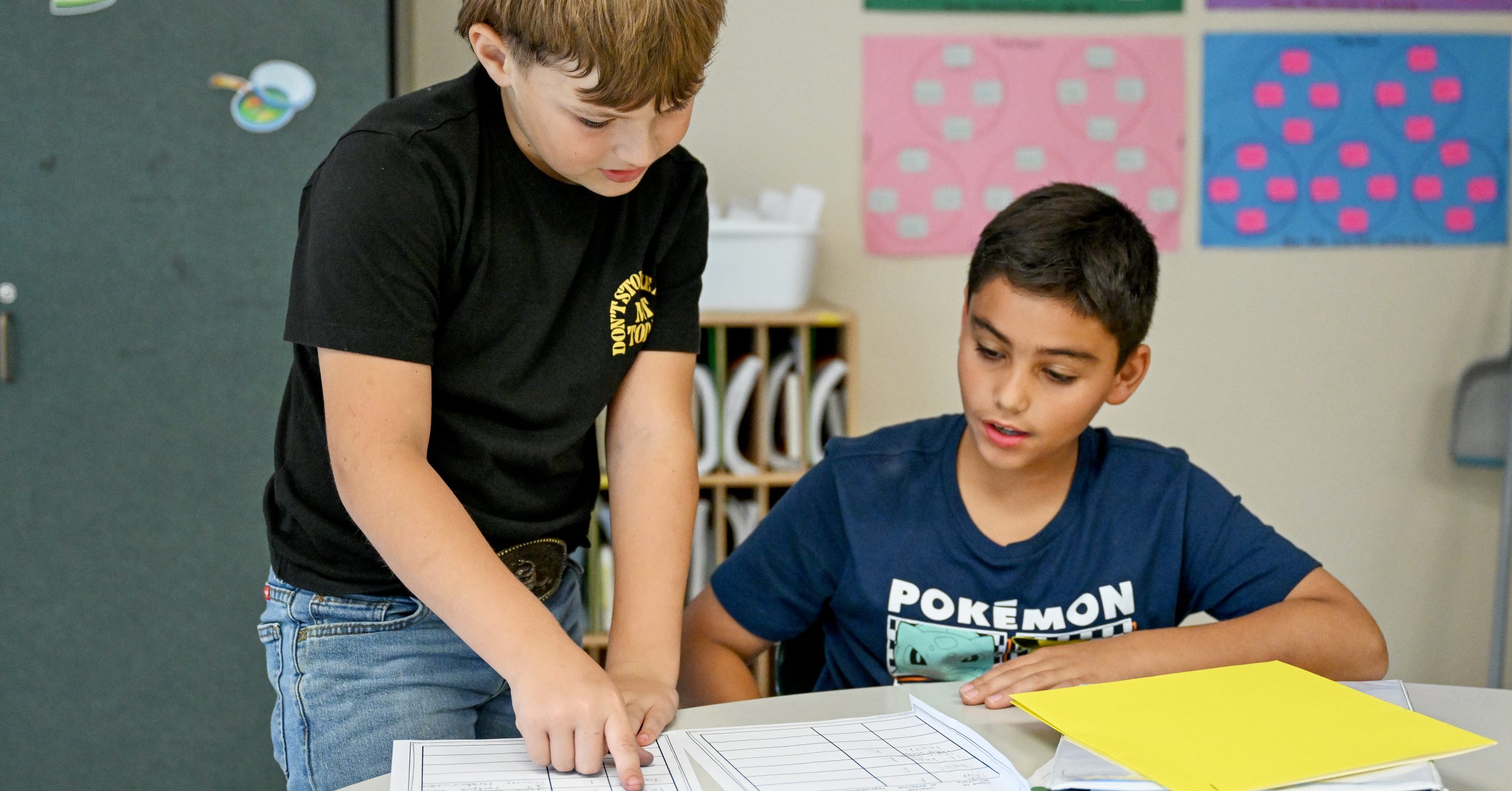 Two students in classroom. One is pointing to something on a sheet of paper.