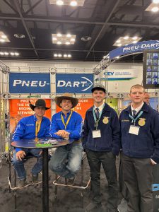 Two men in cowboy hats stand newxt to two Middleburgh students at Pneu-Dart booth.