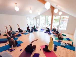 Teen bend and lift arms overhead while sitting on mats at a yoga studio.