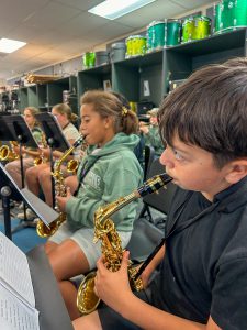 Row of junior high students blowing into brass instruments.