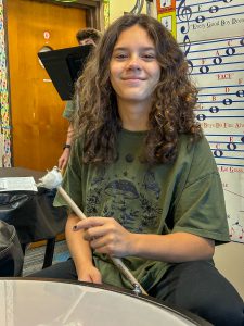 Child in music room. They are holding a drum stick and smiling.