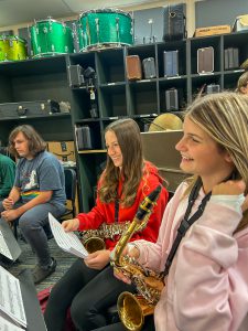 Two girls and one boy sitting with instruments and music in classroom.