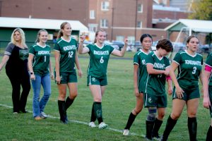 Members of the varisty girls soccer team walk off field with one member giving a victory sign.