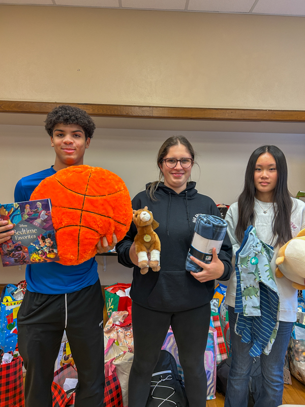 Three students hold up stuffed animals, blankets and pajamas.