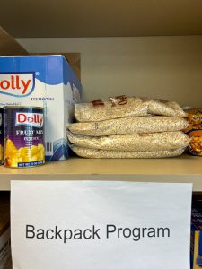 Canned fruit mix and oatmeal on shelf labeled Backpack Program.