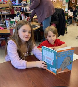 Grade three student reads to pre-kindergarten student at table.