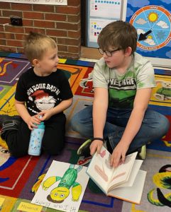 Grade three student exchanges a glance with a pre-kindergarten student. Older student is holding a picture book.