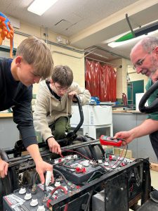 Two students with teacher work on cart restoration project.