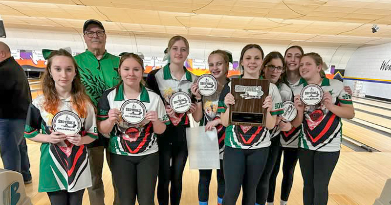 Members of girls varsity bowling team stand with coach at bowling alley. Team members are holding medals.