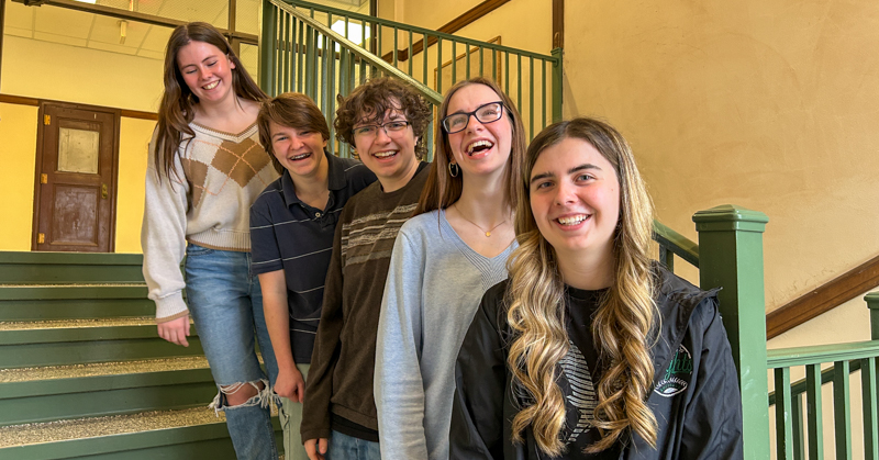 Five high school students standing on stairs. They are smiling and laughing.