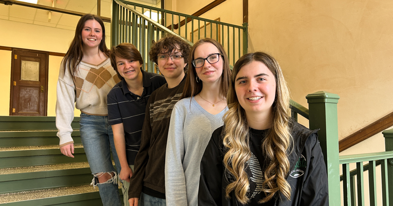 Five students stand on stairwell. Door in background.