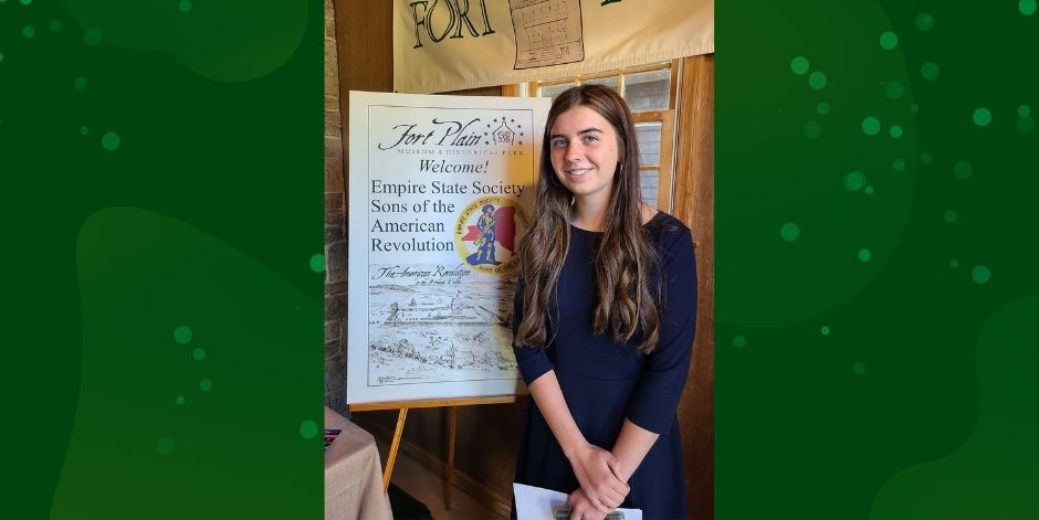 Student stands next to Fort Plain Museum welcome sign.