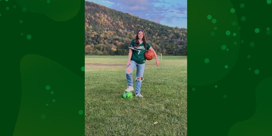 Student stands with basketball and soccer ball. Mountain in background.