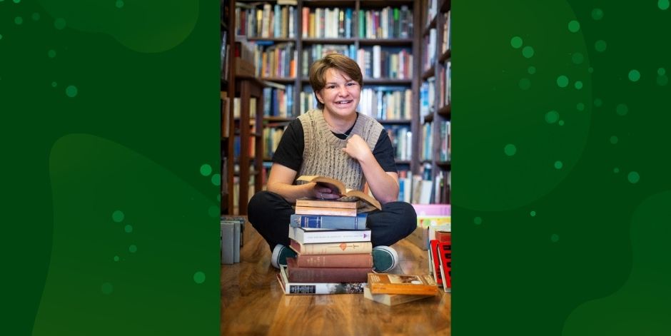 Student sits with pile of books in library.