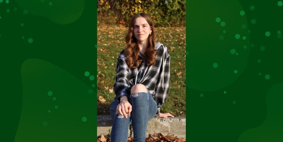 Student sits on curb. Autumn leaves in background.