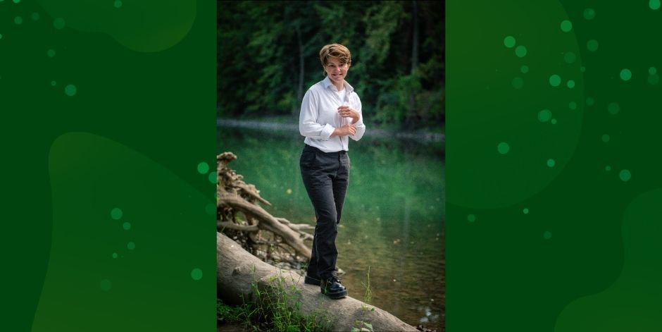 Student walks down fallen log. Stream in the background.