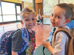 Two little boys with backpacks on in school lobby.